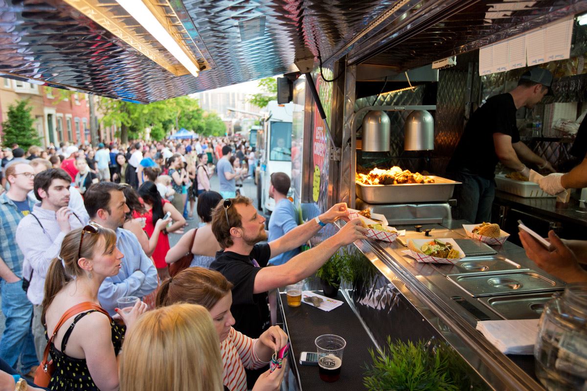 Food truck with customers in line and picking up food from the open window on side of the truck.