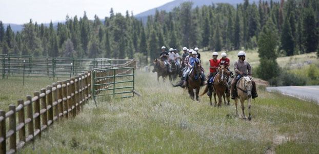 Line of campers on horses riding along side a stall on a ranch
