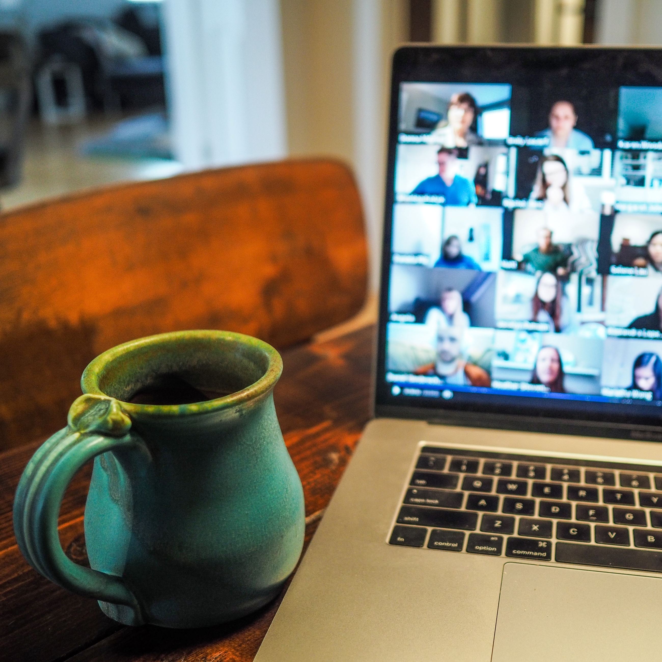 Image of a laptop computer and a mug. The screen shows multiple participants in a virtual meeting.