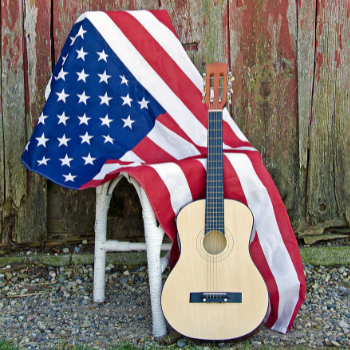 An acoustic guitar leans against a white wicker chair draped in an American flag