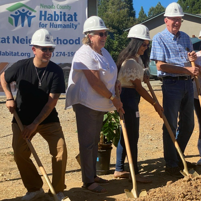 A line of people wearing hard hits dig into the red earth with shovels