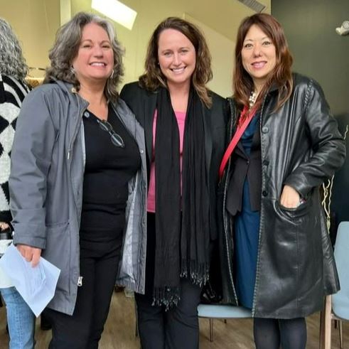 Three women stand together in the Cashin's Field community room smiling at the camera