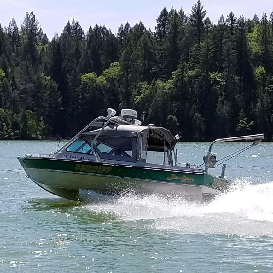 A Nevada County Sheriff's boat glides along the water with tress in the background