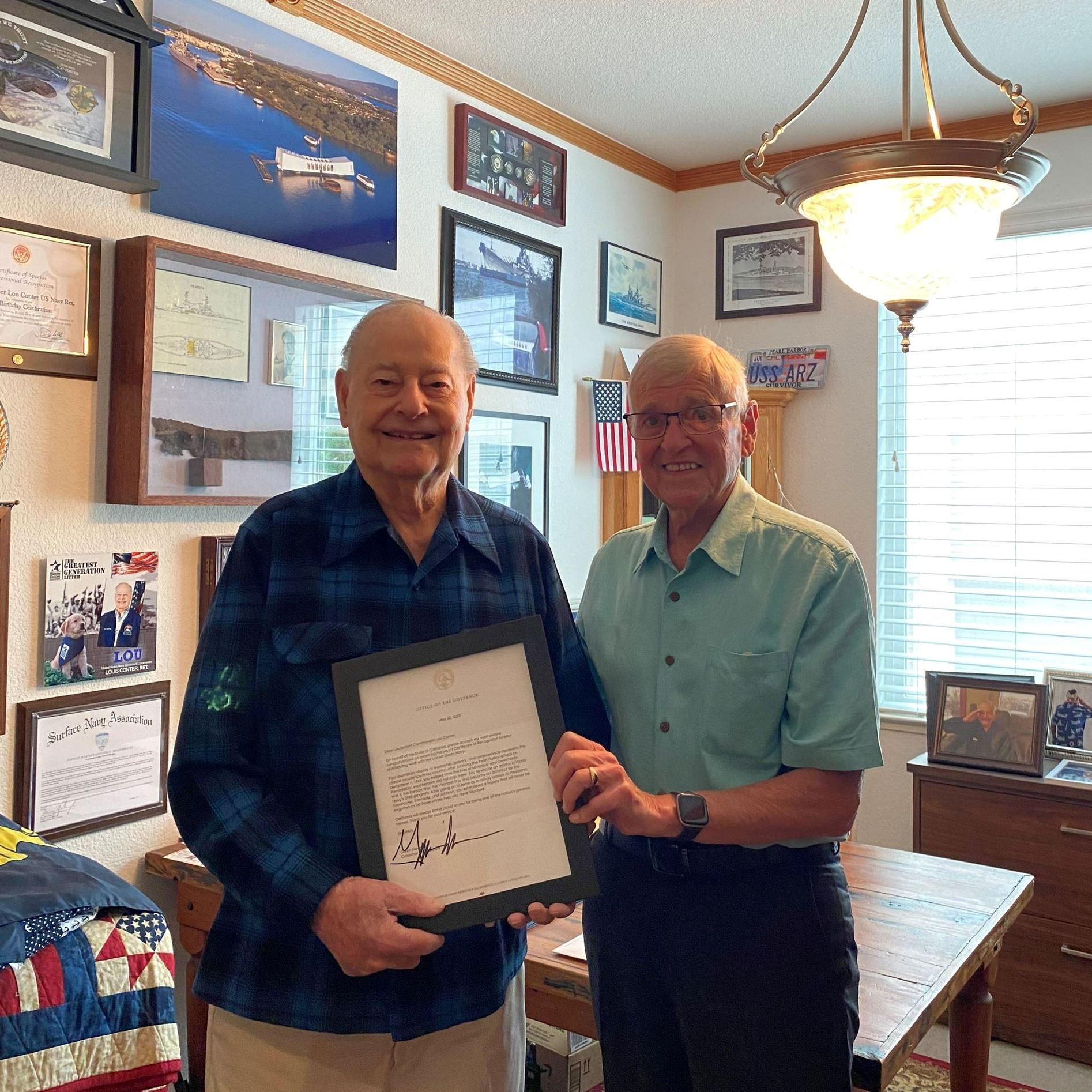 Lou Conter and Supervisor Scofield stand together holding a framed letter.
