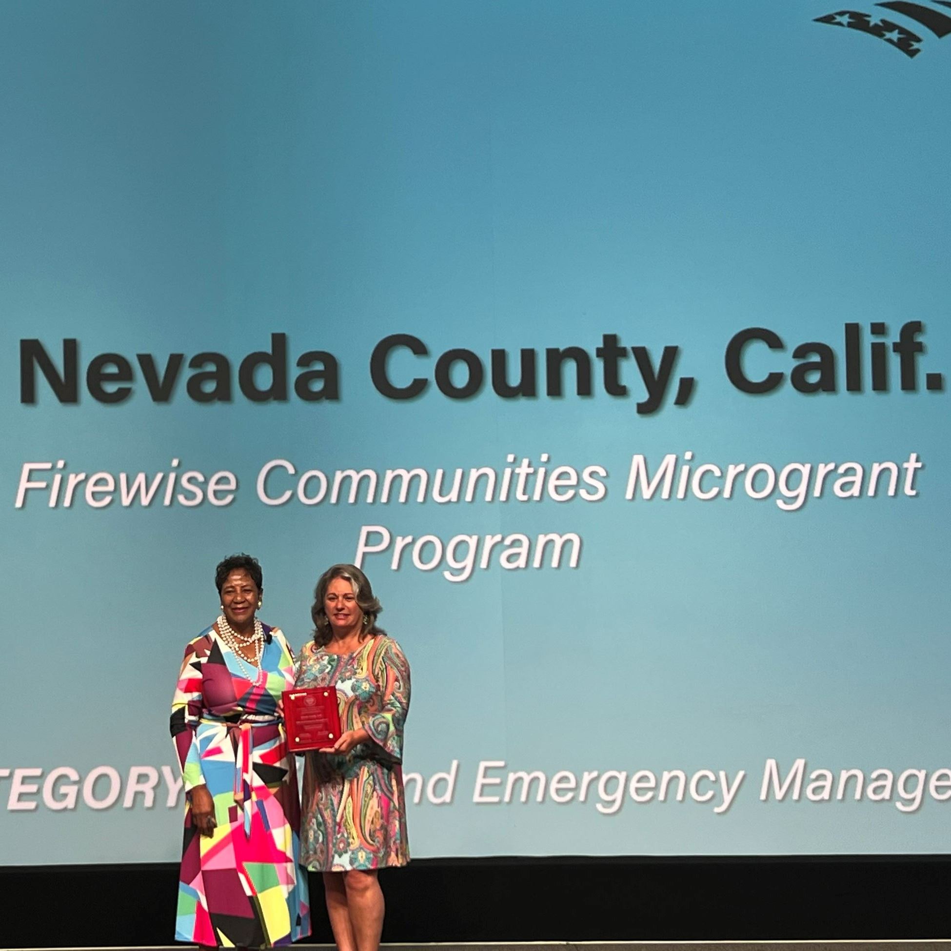 Two people stand on a stage holding an award
