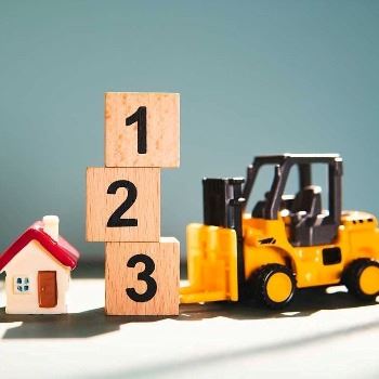 A photo of two houses, with blocks on top of one another numbered 1, 2, & 3, and a forklift