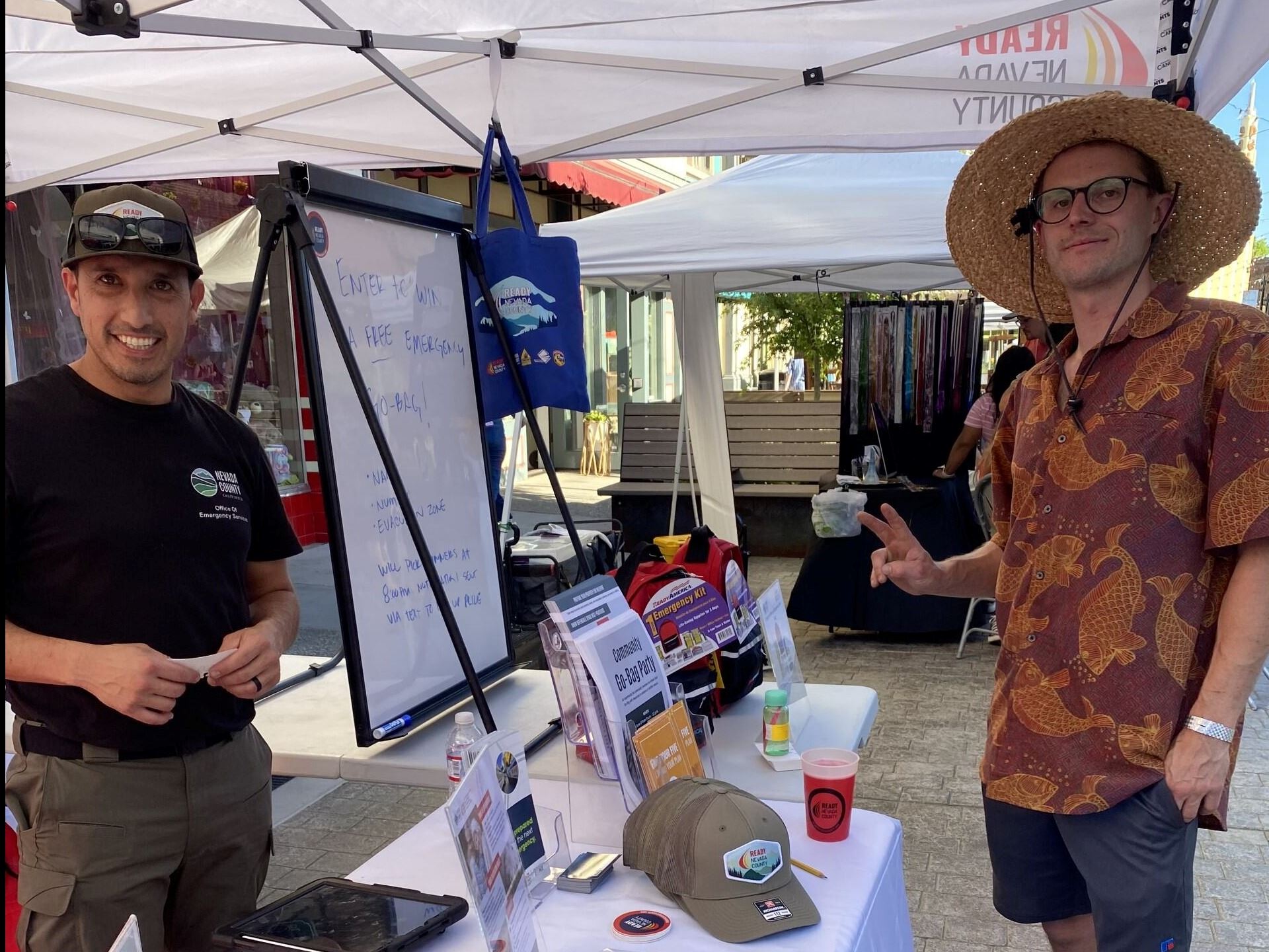 Outreach Booth with OES hats and merch on table with Ready Nevada County sign and resident 
