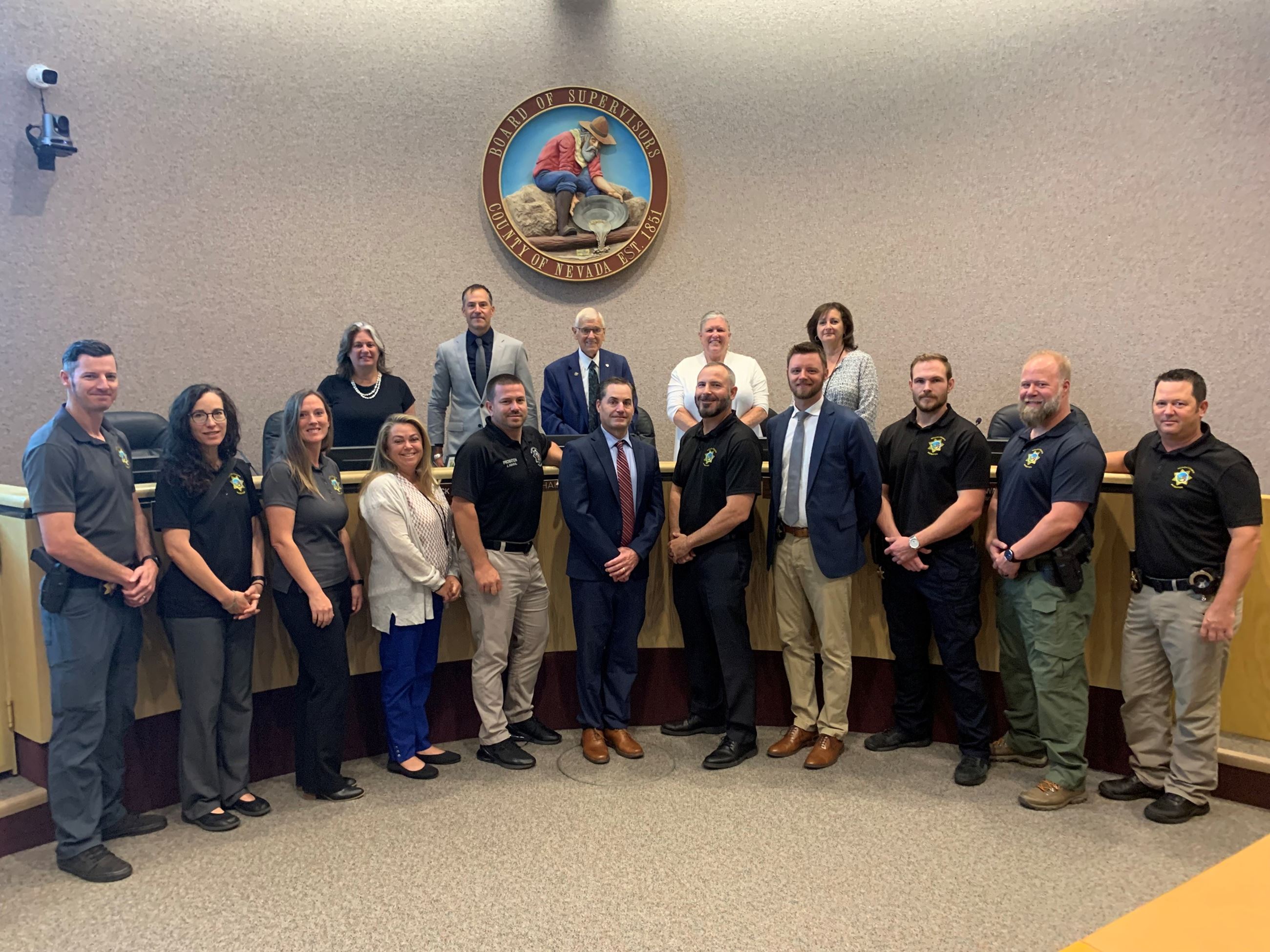 A large group of people stand together in front of  the Nevada County seal